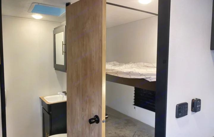 RV rental interior: A compact bathroom with sink and mirrored cabinet, next to a bunk bed sleeping area with controls.. Keystone Springdale 1800BH 2022