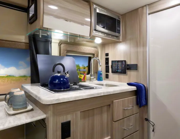 Bright, compact rv rental kitchen featuring light wood cabinetry, a sink, stove, microwave, and a tablet mount. Perfect for travel!. Thor Motor Coach Scope 2022