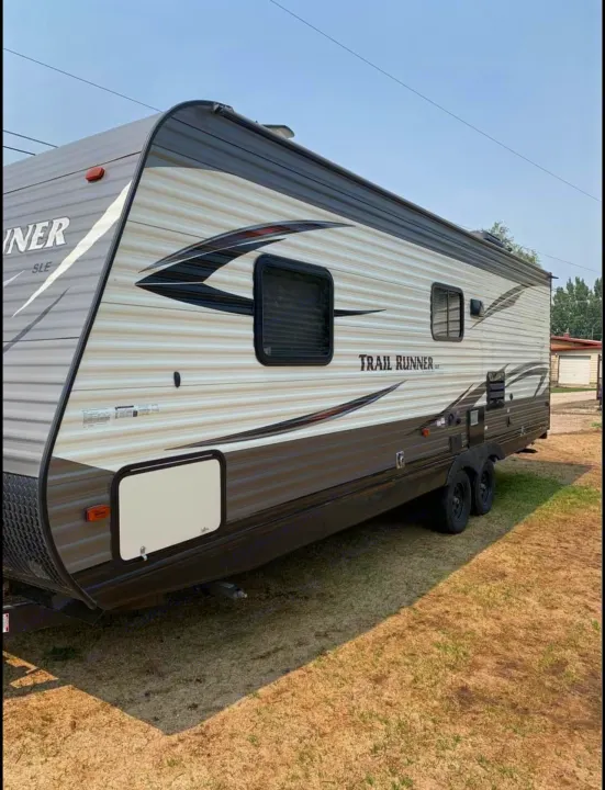 This sleek Trail Runner travel trailer, perfect for an RV rental, is parked on grass, ready for your next adventure.. Heartland RVs Trail Runner SLE 2017