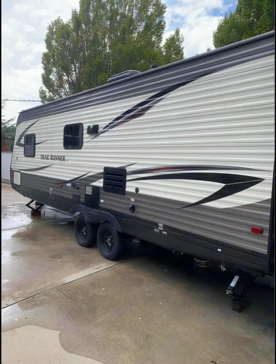 A grey and white travel trailer RV rental, with visible windows and decals, is parked on wet concrete, ready for adventure.. Heartland RVs Trail Runner SLE 2017