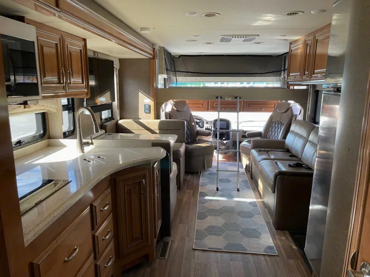 Bright RV rental interior: kitchen with wood cabinets, light counters, cozy seating, and an overhead bunk with ladder.. Thor Palazzo 2019