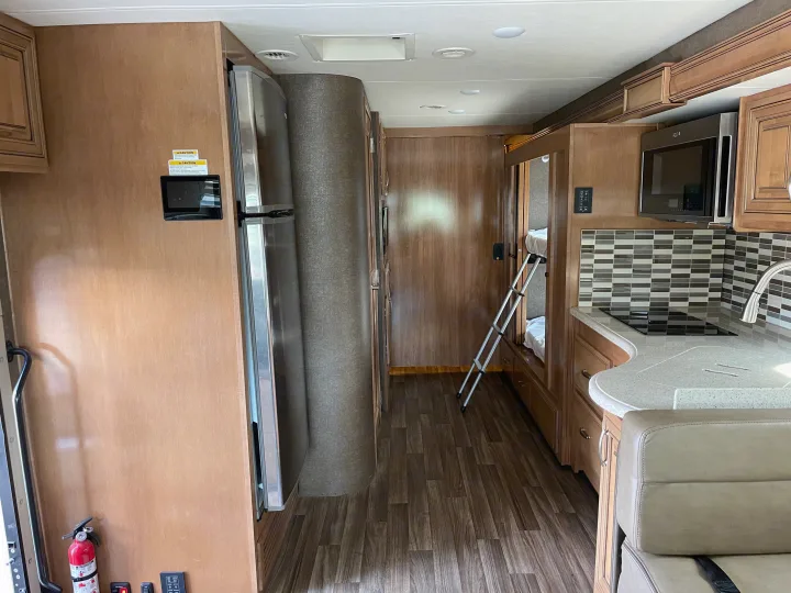 Spacious RV rental interior with a kitchen, refrigerator, bunk beds, wood-look flooring, and light-toned cabinetry.. Thor Palazzo 2019