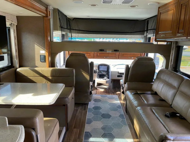 Inside a clean rv rental: dinette, sofa, cockpit, and an overhead bed. Bright, inviting living space.. Thor Palazzo 2019