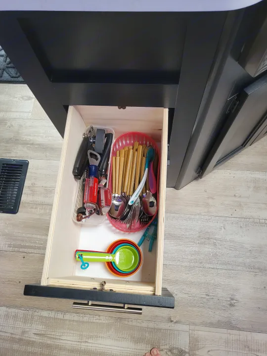 This RV rental's kitchen drawer is open, revealing organized utensils, colorful measuring cups, and various tools, perfect for compact living.. Forest River Cherokee 2021