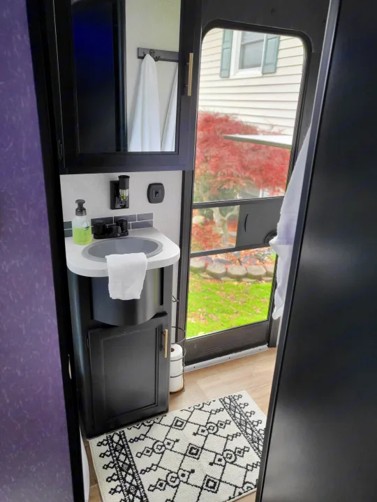 An RV rental's bright interior, featuring a compact sink, window view of a house, and a decorative rug.. Forest River Cherokee 2021