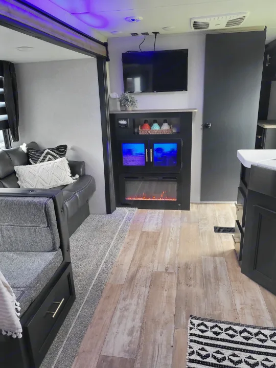 RV rental's modern living area: Enjoy a TV, electric fireplace, beverage cooler with blue light, and comfy sofa on wood-look floor.. Forest River Cherokee 2021