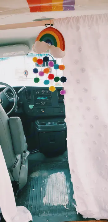 Rainbow mobile and colorful curtain adorn this cozy RV rental interior, showing the driver's area and custom decor.. Chevrolet Express 2018