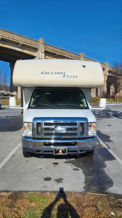 A white Freedom Elite **rv rental** is parked outdoors under a large concrete bridge.. Thor Motor Coach Freedom Elite 2015