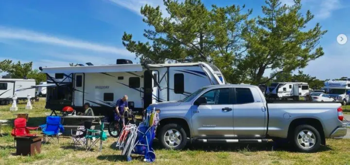 Relaxing at an RV rental campsite with a large travel trailer and pickup truck, surrounded by camping gear and trees.. Cruiser RV Embrace Ultra Lite 2019