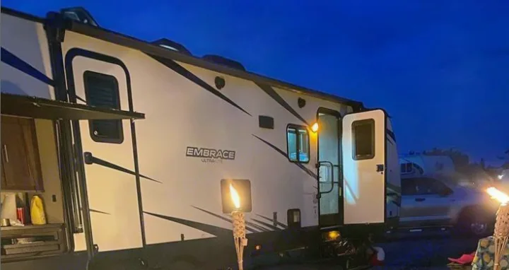 Cozy rv rental camping night: Illuminated Embrace travel trailer with outdoor kitchen, set beside a glowing tiki torch.. Cruiser RV Embrace Ultra Lite 2019