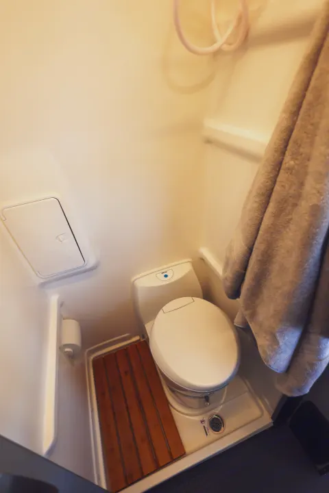 This RV rental's compact wet bath features a white toilet, shower hose, drain, and a practical wooden slatted mat.. Winnebago Revel 2022