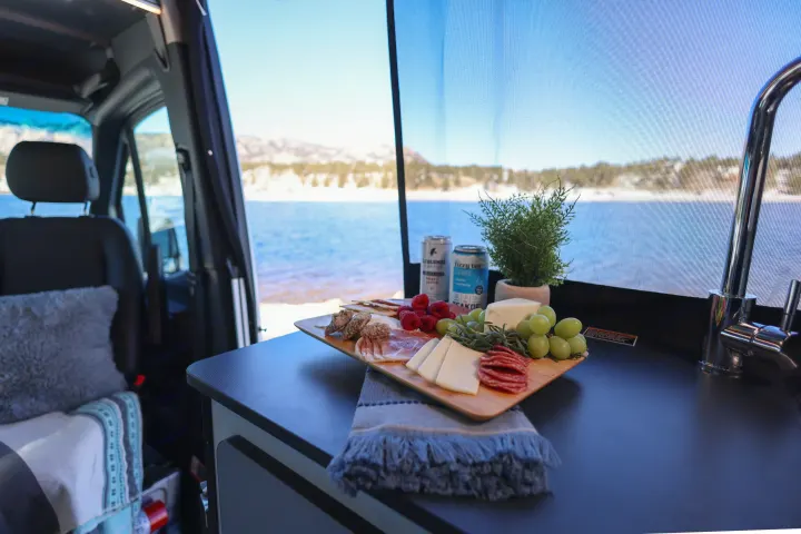 Cozy RV rental interior with a charcuterie board and stunning lake views, perfect for scenic adventures.. Winnebago Revel 2022