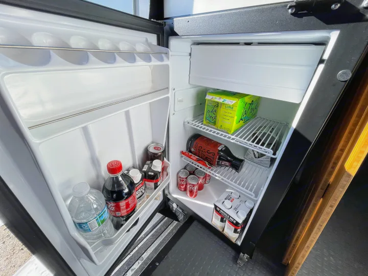 RV rental mini-fridge, neatly stocked with sparkling water, sodas, protein drinks, water, and cold brew coffee.. Winnebago Revel 2022