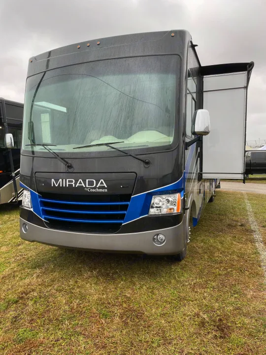A black and blue Coachmen Mirada RV rental, with a side slide-out extended, is parked on a grassy field.. Coachmen Mirada 2018