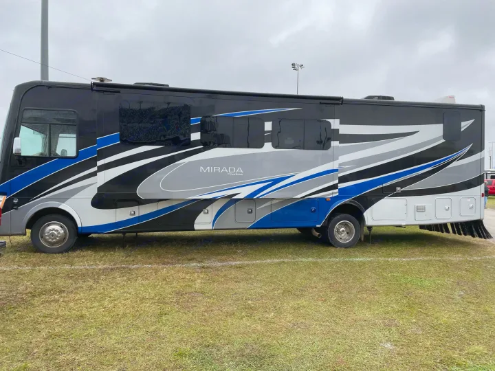 A sleek black, blue, and grey Mirada RV rental parked on grass, ready for adventure. Ideal for your next motorhome travel.. Coachmen Mirada 2018