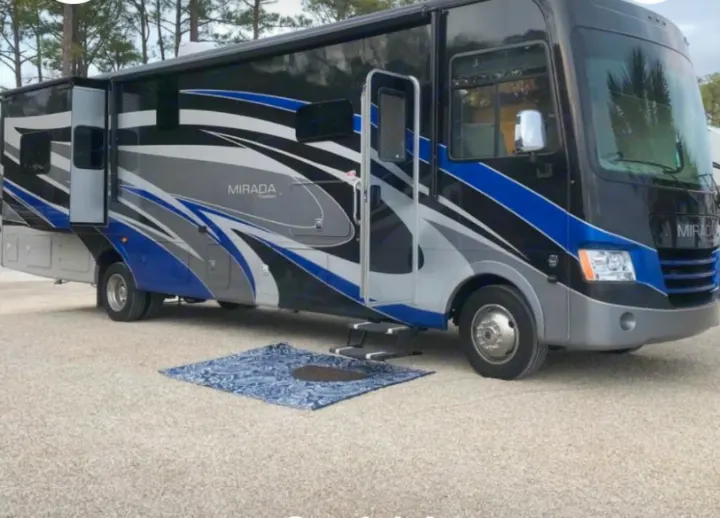 Experience an RV rental! This sleek black, blue & gray motorhome with a slide-out is parked on gravel, ready for travel.. Coachmen Mirada 2018