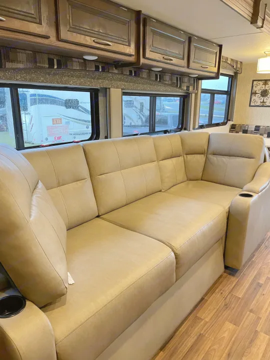 RV rental living area featuring a large tan sectional sofa with cup holders, overhead cabinets, and expansive windows.. Coachmen Mirada 2018