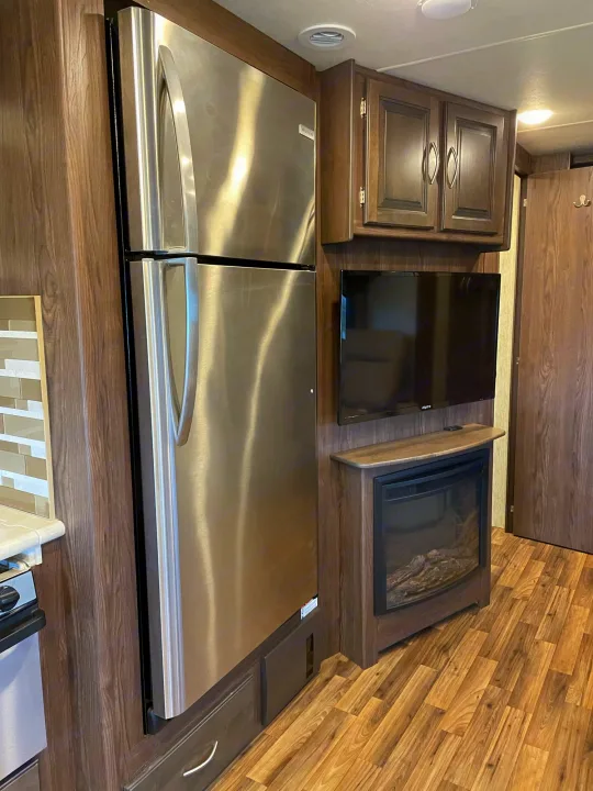 Modern RV rental interior featuring a large stainless steel fridge, wall TV, and electric fireplace.. Coachmen Mirada 2018