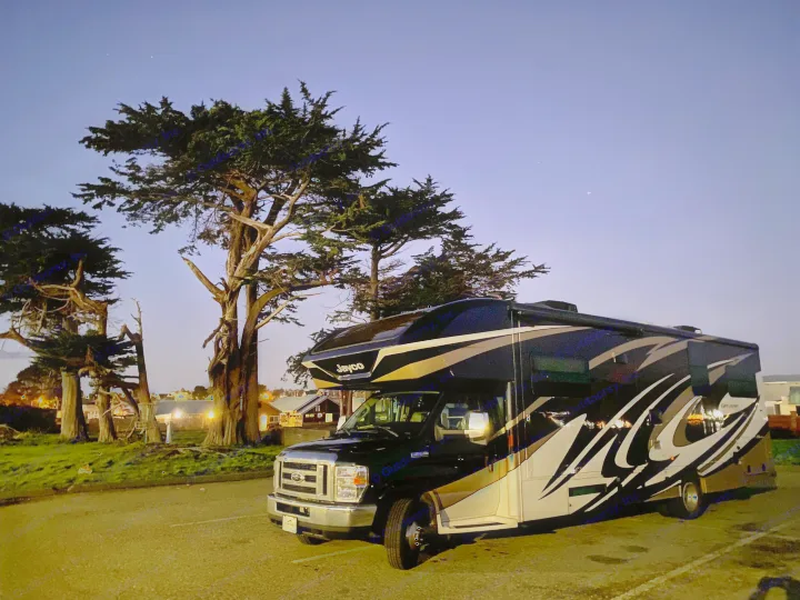 A black and gold Jayco RV rental parked at dusk, with tall trees against a starry blue sky.. Jayco Greyhawk 2018