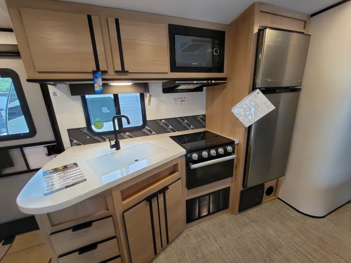 Explore a modern RV rental kitchen featuring a microwave, stove, sink, refrigerator, and light wood cabinetry with black accents.. Cruiser Rv Corp Radiance 30ds 2021