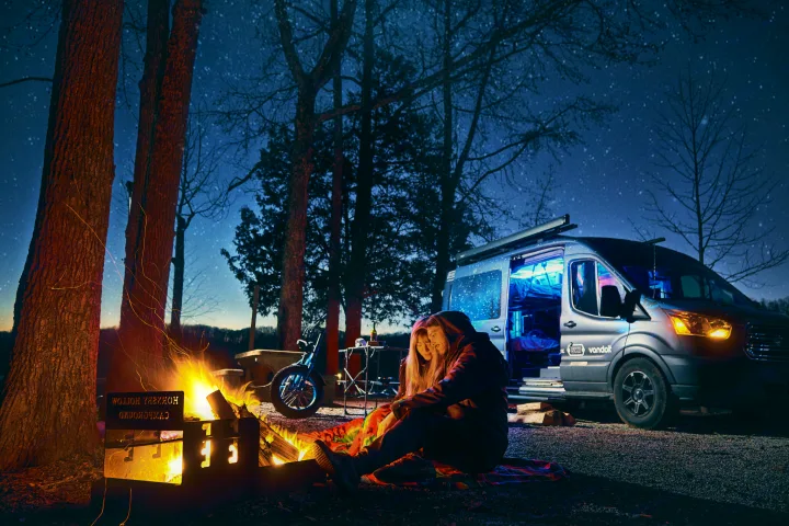 Couple by campfire under starry sky with RV rental camper van. Perfect for nighttime camping adventures.. Ford Transit 2017