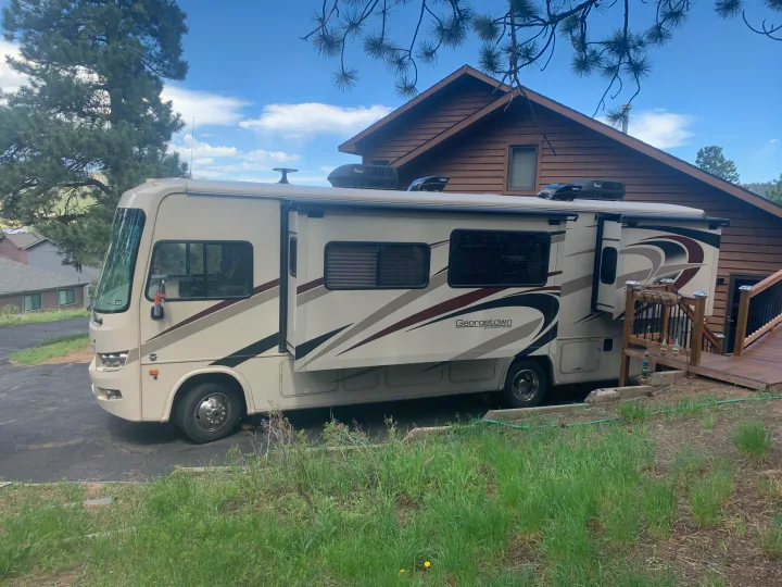 A beige Georgetown RV rental parked next to a rustic house, with slide-outs extended, under a blue sky.. Forest River Georgetown 2019