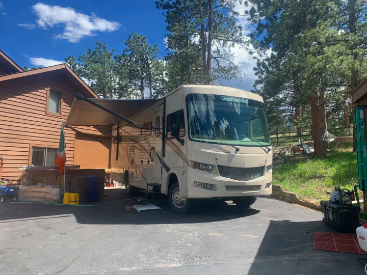 A spacious Georgetown RV rental with its awning extended, parked on a paved driveway next to a house and pine trees.. Forest River Georgetown 2019