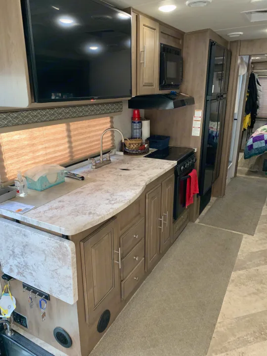 Modern rv rental kitchen featuring a counter, sink, stove, microwave, fridge, and wall-mounted TV. Bedroom beyond.. Forest River Georgetown 2019