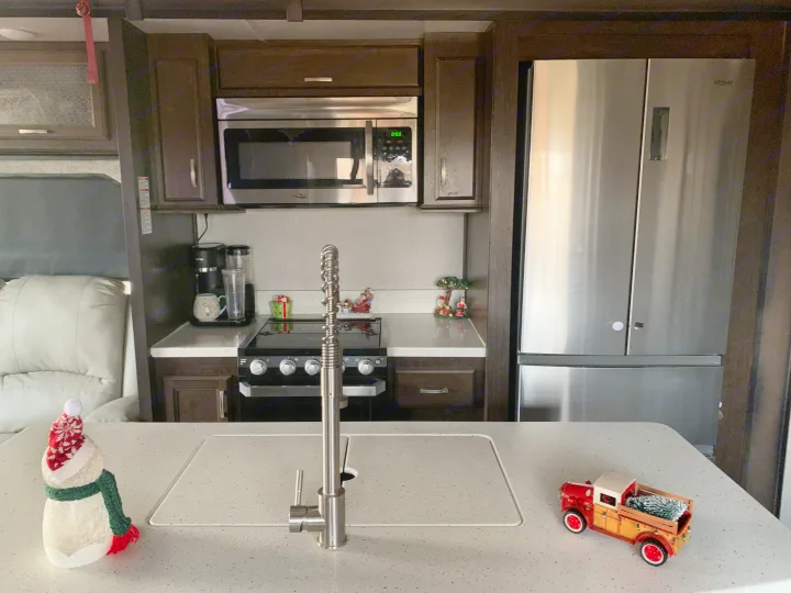 RV rental kitchen: stainless steel appliances (fridge, microwave, stovetop), counter with sink, and festive decor inside a modern RV.. Heartland RVs Elkridge 2019