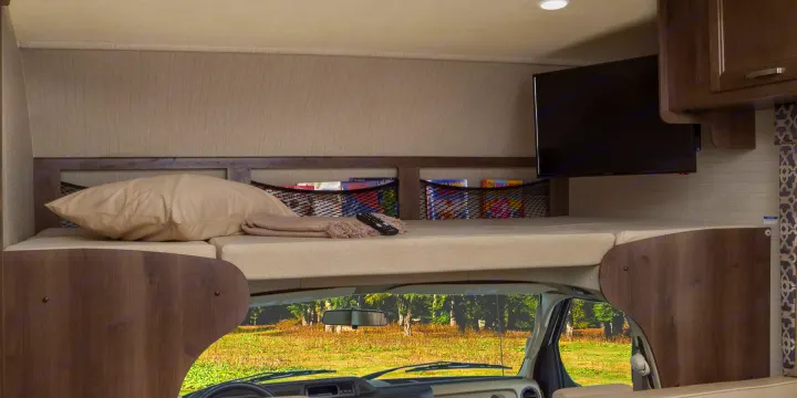 Inside an RV rental: a cozy cab-over bunk with bed, pillow, TV, and handy mesh storage for books, overlooking a scenic view.. Jayco Redhawk 2018