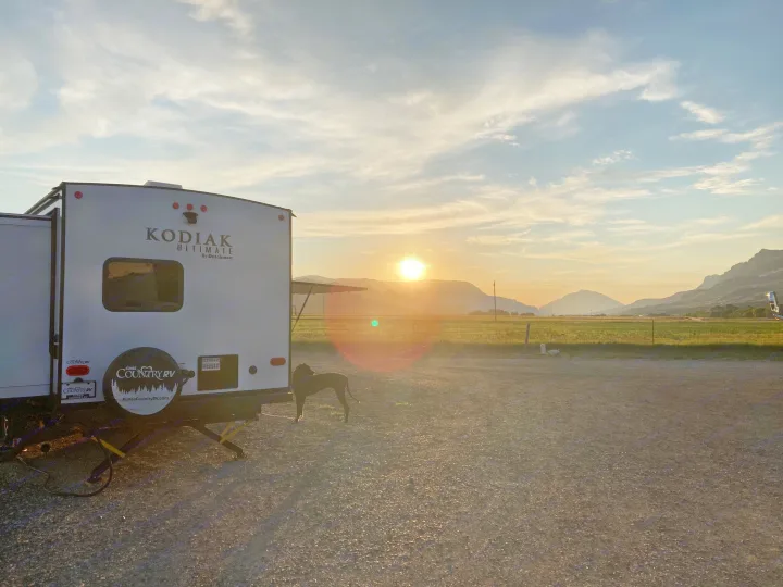 Golden hour at a scenic RV rental site. A white travel trailer & dog face mountains bathed in sunset hues.. Dutchmen Kodiak Ultimate 2020