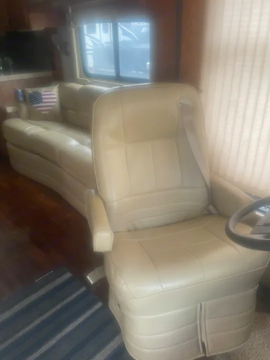 Inside a comfy RV rental: Cream driver's seat, sofa with flag pillow, and window view.. Airstream Skydeck 2008
