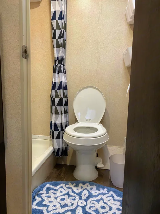 RV rental bathroom with white toilet, modern geometric shower curtain, and a blue patterned rug by the shower stall.. Forest River Salem FSX 2018