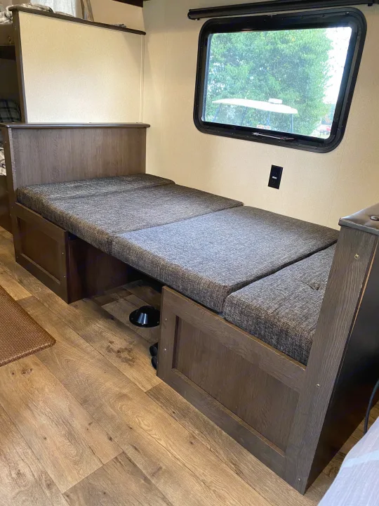 RV rental with a functional interior: a dark wood dinette converts to a comfortable bed with gray cushions. Window view outside.. Forest River Salem FSX 2018