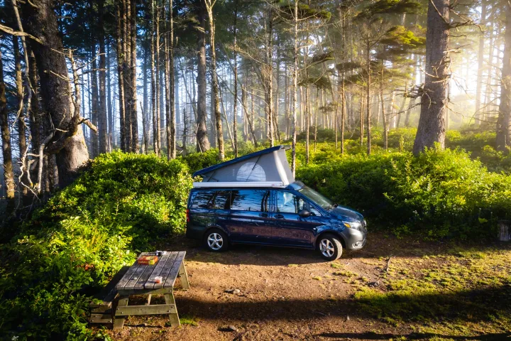 Blue pop-top RV rental parked at a sun-dappled forest campsite with a picnic table ready for a board game adventure.. Mercedes-Benz metris 2022