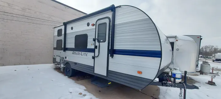 Ameri-Lite travel trailer, great for RV rental, parked on a snowy lot against a brick wall.. Amerilite 197BH 2021