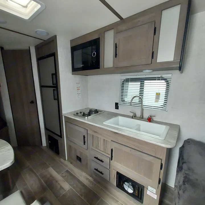 Explore this modern RV rental kitchen: sink, stove, microwave, fridge, and stylish cabinetry for your travels.. Amerilite 197BH 2021