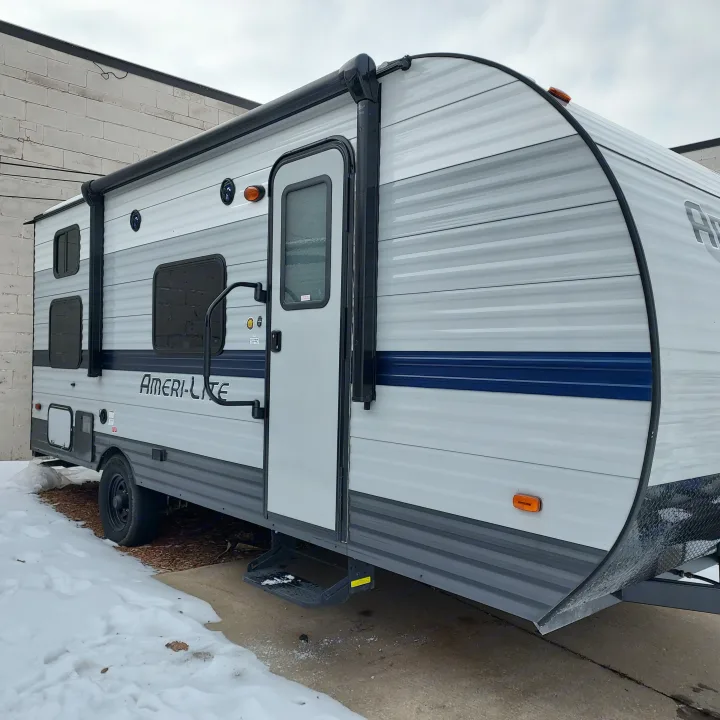 Ameri-Lite RV rental, gray with blue stripe, parked on a snowy lot. Ready for your next adventure.. Amerilite 197BH 2021