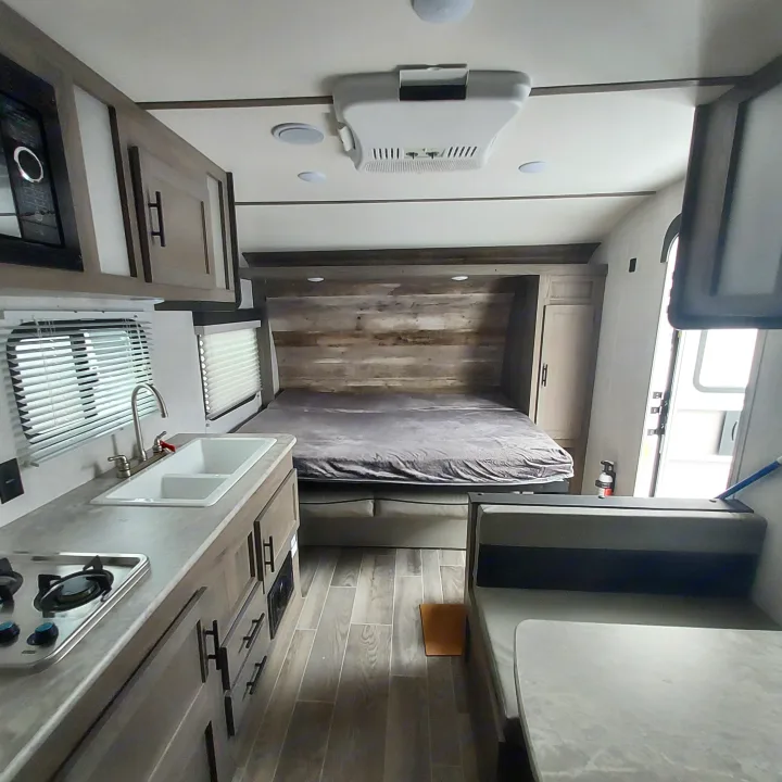 Inside an RV rental, showing a well-equipped kitchen area, a convenient fold-up bed, and sleek interior design.. Amerilite 197BH 2021