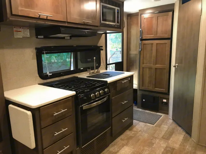 This RV rental's practical kitchen offers a gas range, microwave, sink, fridge, and cabinets. Ideal for travel comfort.. Forest River Rockwood Mini Lite 2020