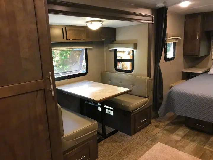 This rv rental interior features a dinette with table & benches, a bedroom, & overhead cabinets. Neutral tones.. Forest River Rockwood Mini Lite 2020