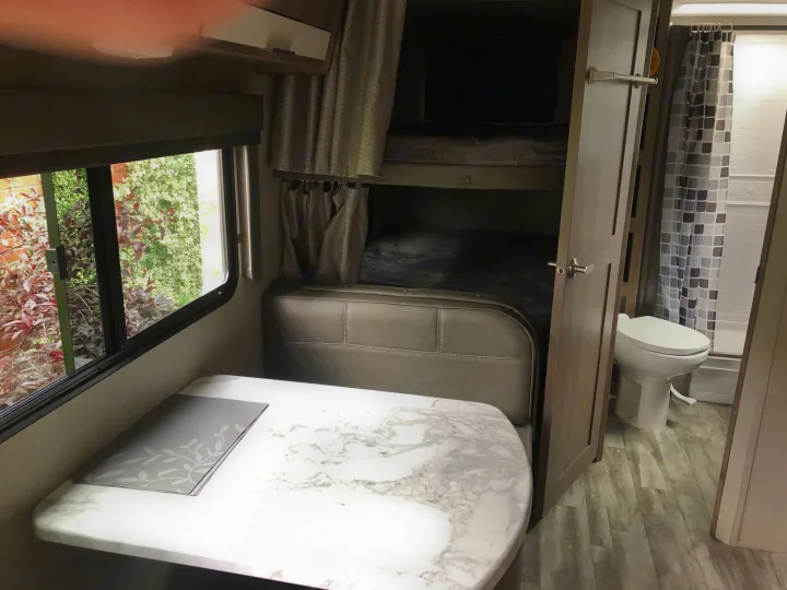 RV rental interior: dinette with table & booth seating, bunk beds, & bathroom with toilet & shower. Wood-look floor.. Grand Design Imagine 23 BHE 2021