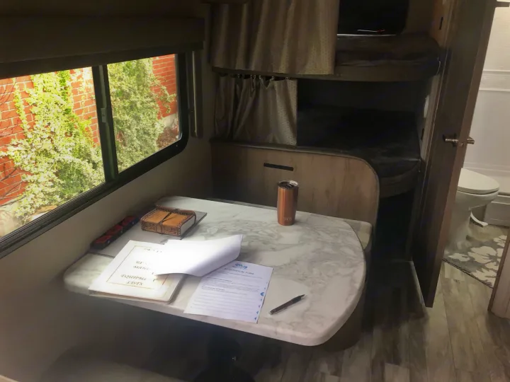 Cozy RV rental interior: dining table with forms, bunk beds with privacy curtains, and an adjacent bathroom. Perfect for road trips.. Grand Design Imagine 23 BHE 2021