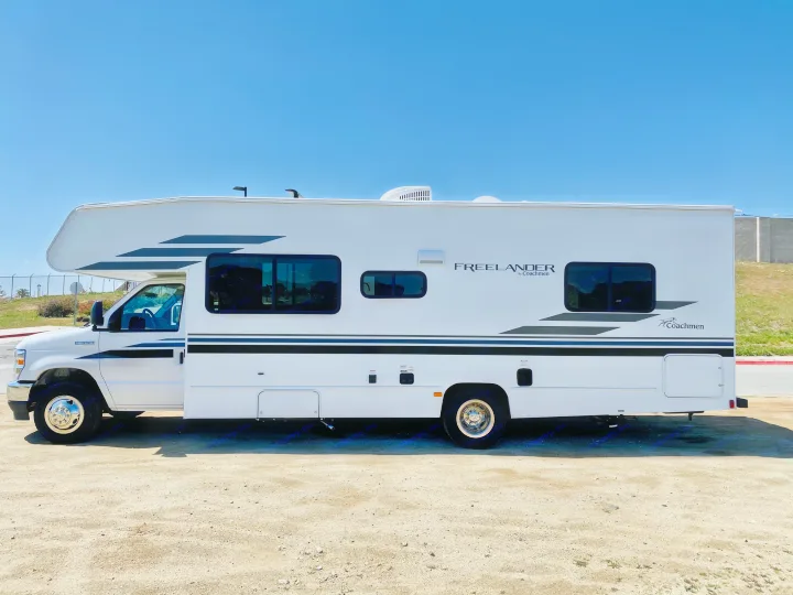 A white Freelander RV rental with black stripes, parked on a dirt lot under a clear sky.. Coachmen Freelander 2021