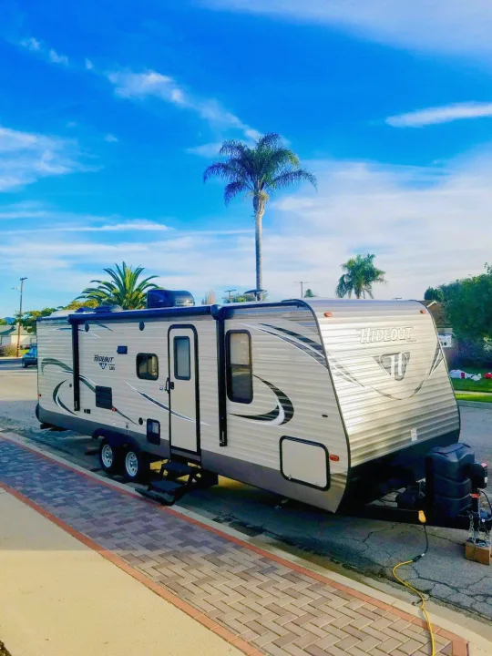 This Hideout travel trailer RV rental is parked on a street under a bright blue sky with palm trees.. Keystone Hideout 2018