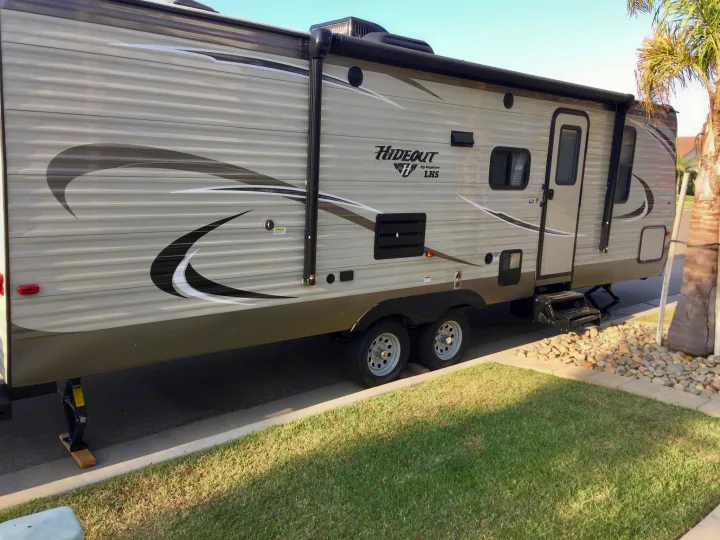 Light-colored Keystone Hideout travel trailer, stabilized by a jack, parked on asphalt. Ideal for an rv rental.. Keystone Hideout 2018