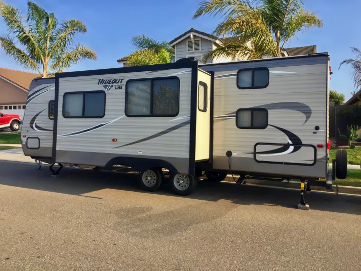 This beige Hideout RV rental, a travel trailer with an extended slide-out, is parked on a residential street.. Keystone Hideout 2018