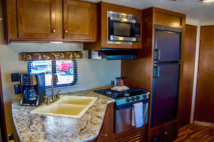 Inside an RV rental: a compact kitchen with sink, coffee maker, stove, microwave, and refrigerator.. Keystone Hideout 2018