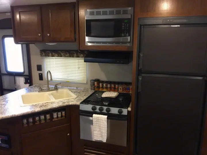 Spacious RV rental kitchen interior featuring a sink, stove, microwave, refrigerator, and organized spice storage.. Keystone Hideout 2018