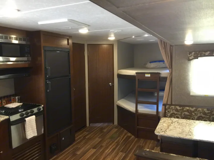 Inside an RV rental: full kitchen with stove/microwave, bunk beds, and dining area. Wood floors & neutral decor.. Keystone Hideout 2018